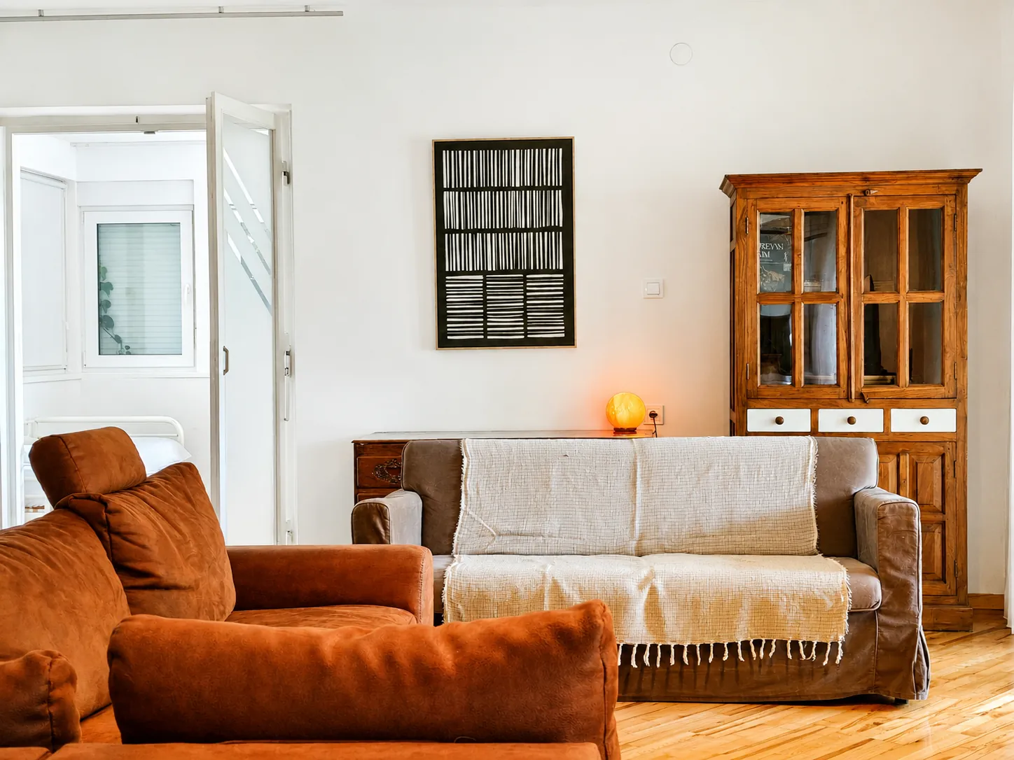 Living area with a terracotta sofa, framed art and a glass-front cabinet