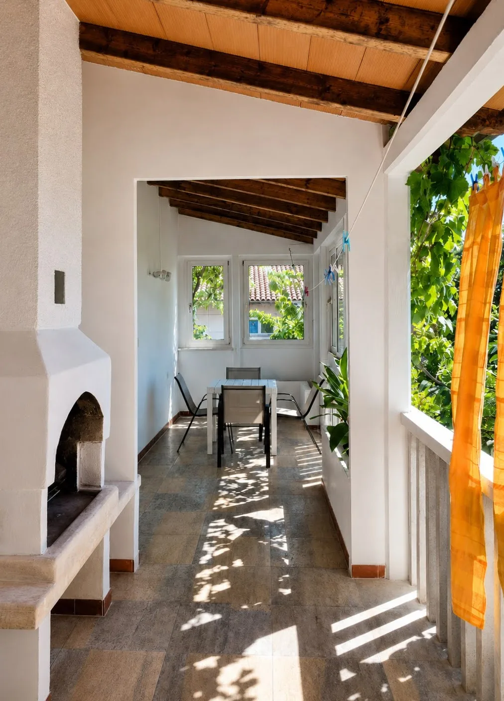 Covered terrace with a built-in stone grill, a table for four, and a beamed roof